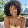 Illustrative photo of a young woman with curly hair in a yellow top, the CN Tower behind her