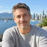 Illustrative photo of a man in a grey sweater, water and mountains behind him
